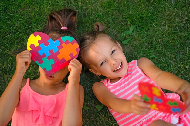 Dziewczyny leżą na trawie i bawią się kartkami w kształcie serca z przyklejonymi kawałkami układanek w środku.