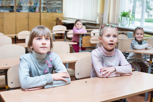 Dziewczyny siedzą przy szkolnej ławce i uważnie słuchają nauczyciela