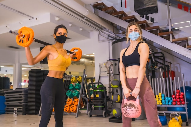Dziewczyny trenują mięśnie z ciężarami z maskami na twarz, dystansem społecznym i nową normą
