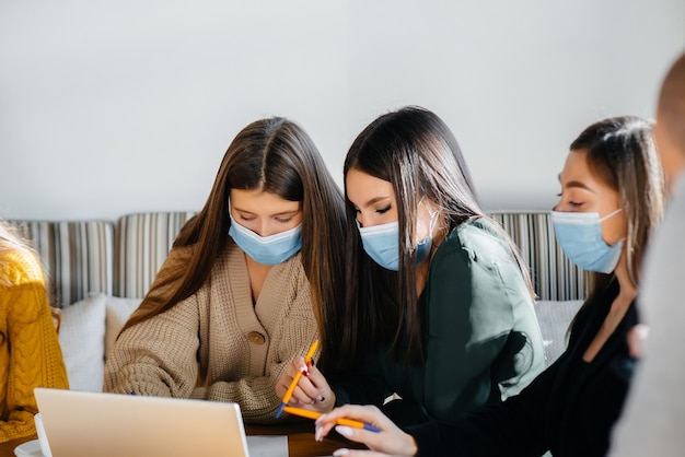 Dziewczyny w maskach siedzą w biurze i pracują na laptopie.