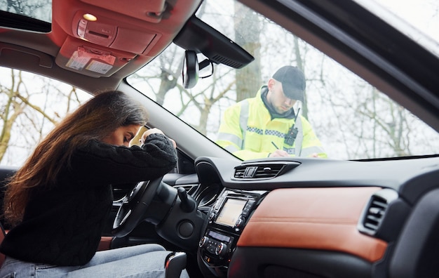 Dziewczyny źle się czują. Mężczyzna policjant w zielonym mundurze sprawdzania pojazdu na drodze.