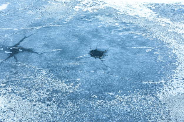 Dziura z pęknięciami w lodzie na zamarzniętej powierzchni rzeki Zimowe tło i tekstura lodu