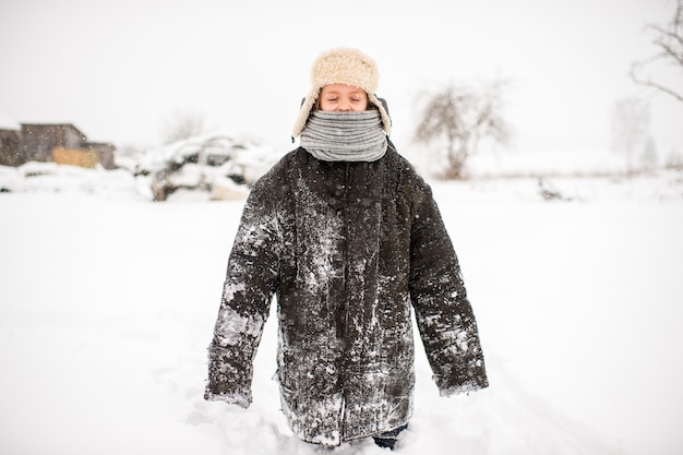 Dziwna Mała Dziewczynka W Znoszonych Zbyt Dużych Ubraniach Stojąca Przy Zaśnieżonej Drodze W Zimowy Dzień W Rosyjskiej Wiosce