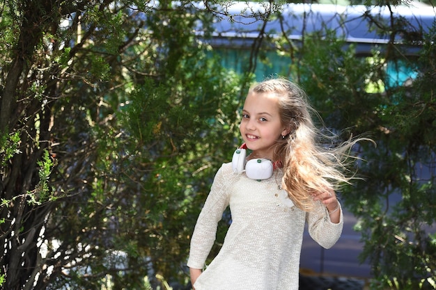 Dźwięk muzyki w mp3 Szczęśliwa dziewczyna tańczy do muzyki w letnim parku Małe dziecko słucha muzyki w słuchawkach na zewnątrz Uśmiechnięty tancerz z długimi rozwianymi włosami Letnia zabawa i radość