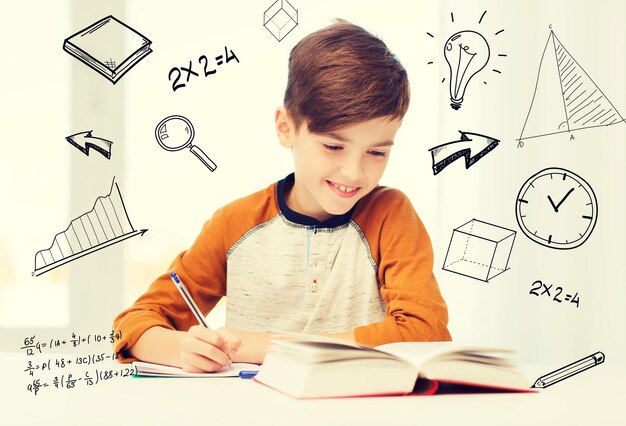 Zdjęcie edukacja, dzieciństwo, ludzie, praca domowa i koncepcja szkoły - uśmiechnięty uczeń z książką piszącą do notatnika w domu nad matematycznymi bazgrołami