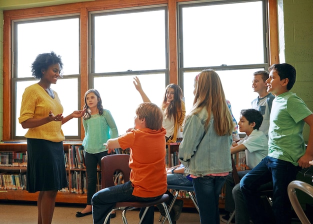 Edukacja edukacyjna i uczeń z pytaniami dla nauczyciela w klasie gimnazjum Biblioteczna grupa stypendialna i uczeń płci męskiej podnoszący rękę, aby odpowiedzieć na pytanie studiując lub pomagając czarnej kobiecie