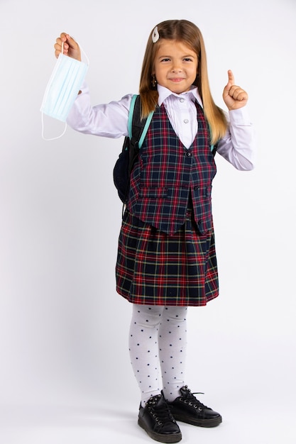 Edukacja podczas kwarantanny. Dziecko dziewczynka w mundurze wskazuje palcem na bok, na białym tle na szarej ścianie.