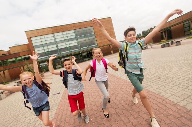 edukacja podstawowa, przyjaźń, dzieciństwo i koncepcja ludzi - grupa szczęśliwych uczniów szkół podstawowych z plecakami biegającymi i machającymi rękami na zewnątrz