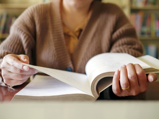 Zdjęcie edukacja uczenia się ręka starszej kobiety siedzącej i czytającej książkę fikcyjną na drewnianym stole