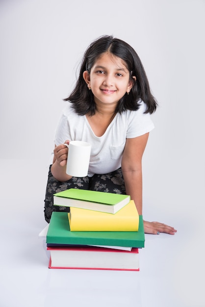 Edukacja w domu koncepcja - Cute little indyjskich lub azjatyckich dziewczyna studiuje ze stosem książek i kubek kawy, siedząc na podłodze w domu. Pojedynczo na białym tle