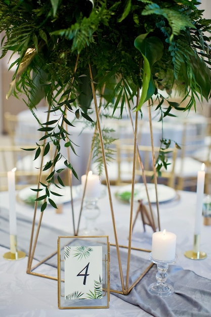 Egzotyczna kompozycja kwiatowa ze świeczkami z liści palmowych i numerem stołu na weselnym stole