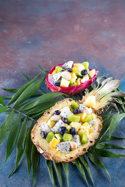 Zdjęcie egzotyczna owocowa sałatka słuzyć w połówce ananas na palmowych liściach na kamiennym tle. zdrowe jedzenie