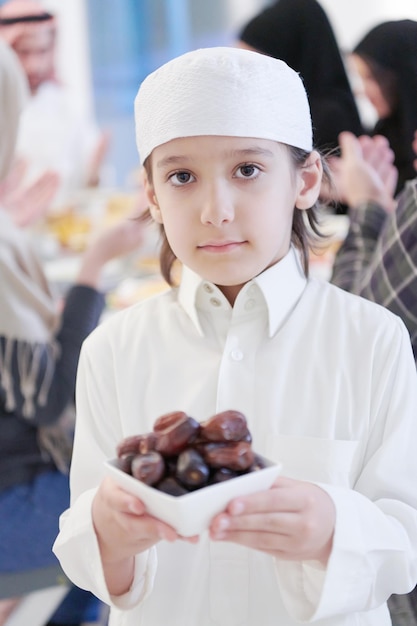 Eid Mubarak Muzułmańska rodzina je obiad iftar mały chłopiec trzyma talerz pełen słodkich daktyli, aby przerwać ucztę. Jedzenie tradycyjnych potraw podczas miesiąca biesiadowania Ramadanu w domu. Islamskie jedzenie halal i