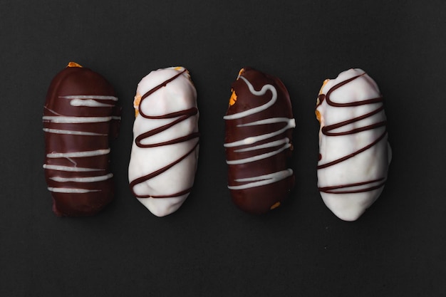 Eklery z nadzieniem czekoladowym i białą czekoladą na czarnej powierzchni.
