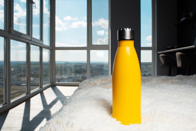 Ekologiczna butelka wielokrotnego użytku w kolorze żółtym na tle panoramicznego okna