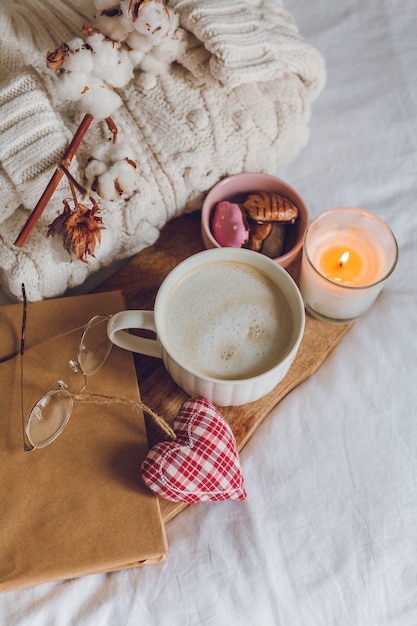 Zdjęcie ekologiczny wystrój domu. domowy przytulny wystrój. kubek cappuccino, ciasteczka, świeca na łóżku. zimowy poranek. wakacje.