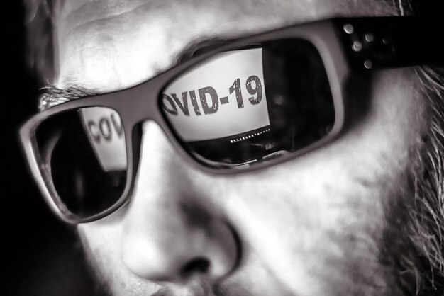 Zdjęcie ekran komputera koncepcyjnego koronawirusa covid19 z ostrzeżeniem covid19 odbija się w męskich okularach
