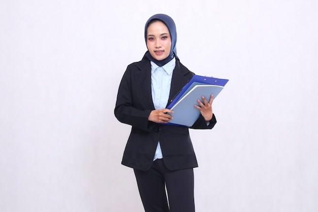 Ekskluzywna azjatycka kobieta z biura w hidżabie stoi uśmiechnięta wesoło niosąc tabliczkę z piórem i