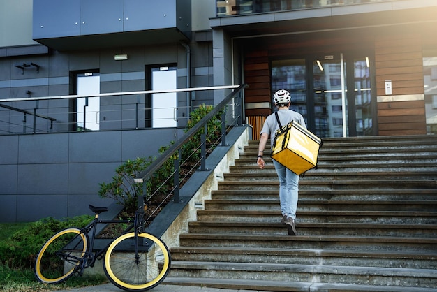 Ekspresowa dostawa kurier z izolowaną torbą wchodząc po schodach po zaparkowaniu roweru