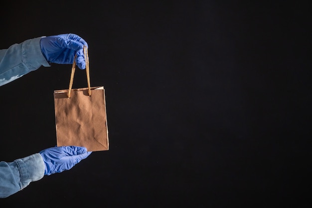 Ekspresowa dostawa na epidemię koronawirusa Zbliżenie rąk kuriera w gumowych rękawiczkach z papierową torbą z uchwytami Opakowanie wykonane z ekologicznego materiału pochodzącego z recyklingu Darowizna na kwarantannę