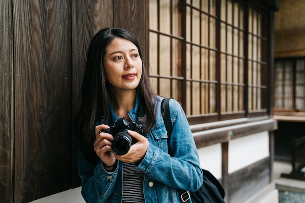 Elegancka Azjatycka Fotografka Opierająca Się Na Drewnianej ścianie I Patrząca Na Innych Z Aparatem W Dłoni. Podróży Japonia Letnie Wakacje Dziewczyna Korzystających Z Kultury Japońskiej. Kioto Podróżuje Turysta Kobieta Na Va