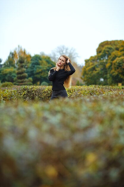 Zdjęcie elegancka blondynka w swetrze pozuje w ogrodzie botanicznym