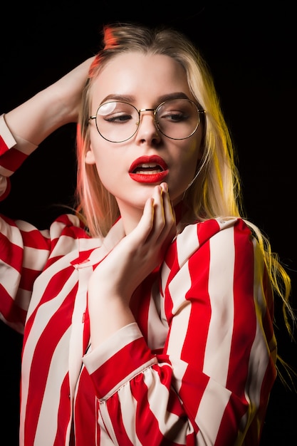 Elegancka blondynka z czerwonymi ustami, w okularach, pozuje z czerwonym i żółtym światłem w studio