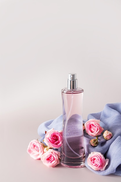 Elegancka butelka kosmetyków na tle szarego szyfonowego szalika damskiego z żywymi pąkami róż Pionowe pastelowe tło Miejsce na kopię