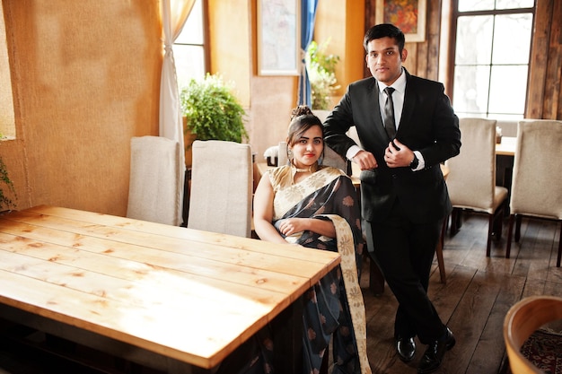 Elegancka i modna indyjska para przyjaciół, kobieta w sari i mężczyzna w garniturze, pozowała wewnątrz kawiarni