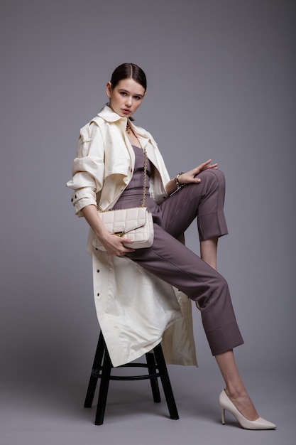 Elegancka kobieta w ładnym białym płaszczu fioletowa górna torebka akcesoria do spodni na szarym tle