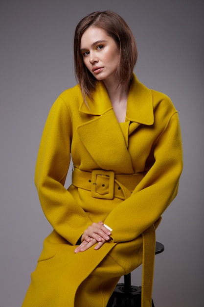 Elegancka kobieta w ładnym żółtym musztardowym płaszczu, czarne botki na szarym tle Fryzura Bob