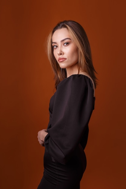 Elegancka młoda azjatycka modelka ubrana w czarną sukienkę pozowanie na pomarańczowym tle