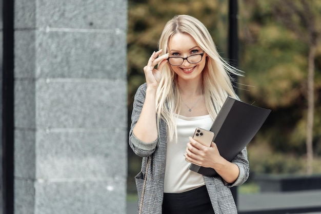 Elegancka młoda blond kobieta biznesu z folderem w budynku biurowym na zewnątrz