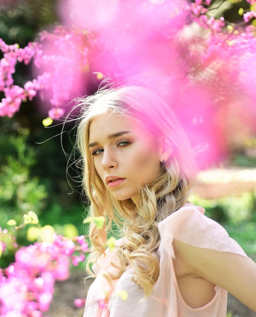 Elegancka młoda dama korzystających z spaceru w kwitnącym ogrodzie, koncepcja wiosna czas. Portret pięknej dziewczyny z długimi, blond, kręconymi włosami na naturalnym tle wśród różowych kwiatów