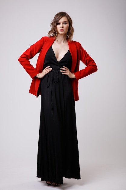 Elegancka młoda kobieta w czarnej sukni wieczorowej z czerwoną kurtką z głębokim dekoltem na białym tle