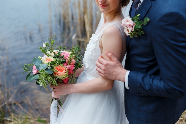 Elegancka panna młoda w białej sukni z koronką trzymająca ślubny bukiet kwiatów i pana młodego w niebieskim garniturze