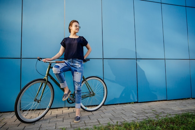 Elegancka piękna dziewczyny pozycja z rocznika rowerem i patrzeć daleko od, blisko błękitnej ściany, cieszy się wolny czas outdoors.