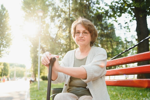 Elegancka starsza kobieta w koszuli siedzi na ławce w parku w ciepły dzień