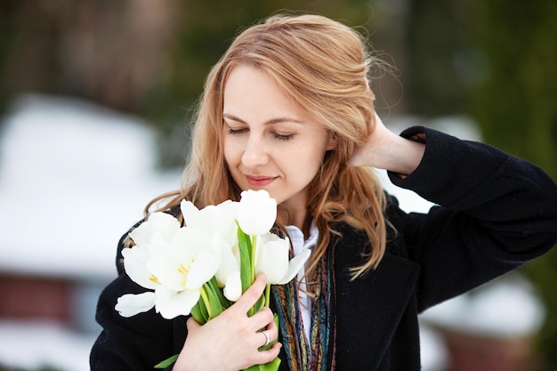 Zdjęcie elegancka zamyślona młoda kobieta z długimi blond włosami w czarnym płaszczu pozuje w mieście