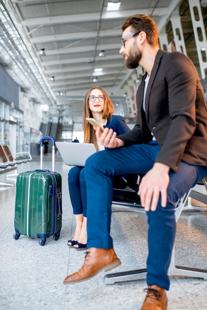 Zdjęcie elegancki biznes para siedzi z laptopem i bagażem w poczekalni na lotnisku. rozmowa biznesowa podczas podróży na lotnisku