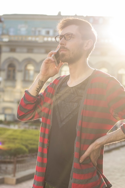 Elegancki mężczyzna opowiada na telefonie komórkowym outdoors. Hipster używa smartfona na ulicy miasta