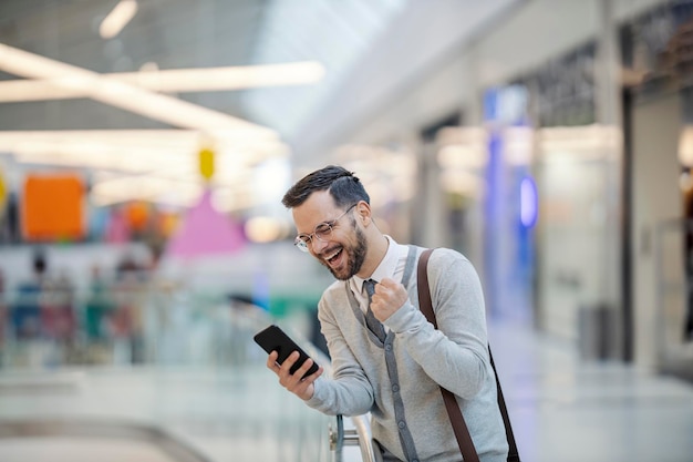 Elegancki mężczyzna stoi w centrum handlowym z telefonem i świętuje podwyżkę