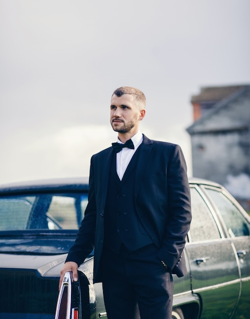 Elegancki mężczyzna w stroju w pobliżu starego samochodu