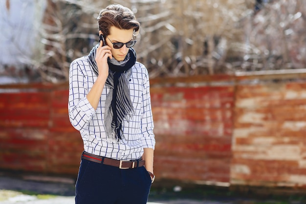 Elegancki młody człowiek w okularach przeciwsłonecznych z telefonem na ulicie
