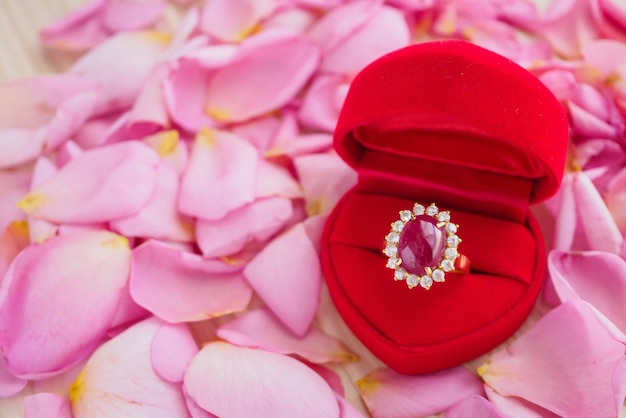 Elegancki pierścionek z rubinem w pudełku z biżuterią w czerwonym sercu na pięknym różowym tle płatków róży z bliska