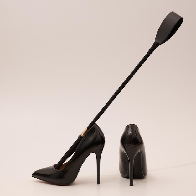 Eleganckie drogie czarne buty damskie na wysokim obcasie z szpicrutą na tle fetysz kobiecej broni