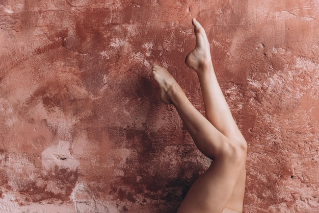 Eleganckie kobiece nogi Młoda dziewczyna wykonuje ćwiczenia gimnastyczne, podnosząc swoje opalone, piękne nogi i opierając je o ścianę