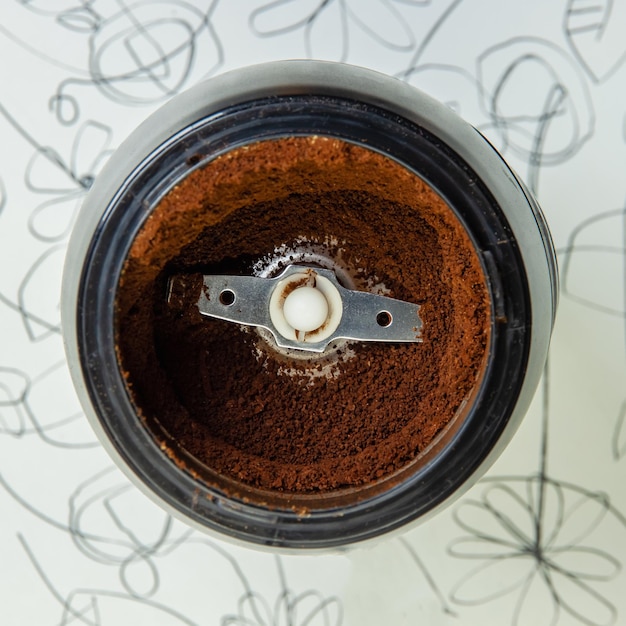 Zdjęcie elektryczna młynka do kawy z świeżo zmiażdżoną kawą na białym stoliku