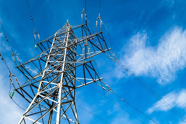 Elektryczna wieża wysokiego napięcia z przewodami na zachmurzonym tle błękitnego nieba w słoneczny dzień