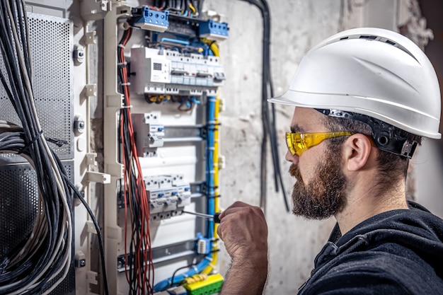 Elektryk Mężczyzna Pracuje W Rozdzielnicy Z Elektrycznym Kablem Połączeniowym, łączy Sprzęt Z Narzędziami.